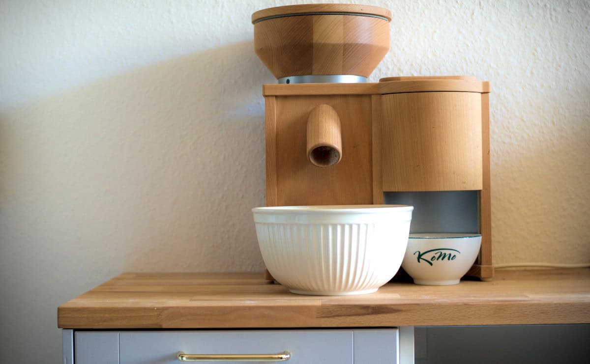 wooden grain mill and white ceramic bowl under the spout sitting on a wooden kitchen counter