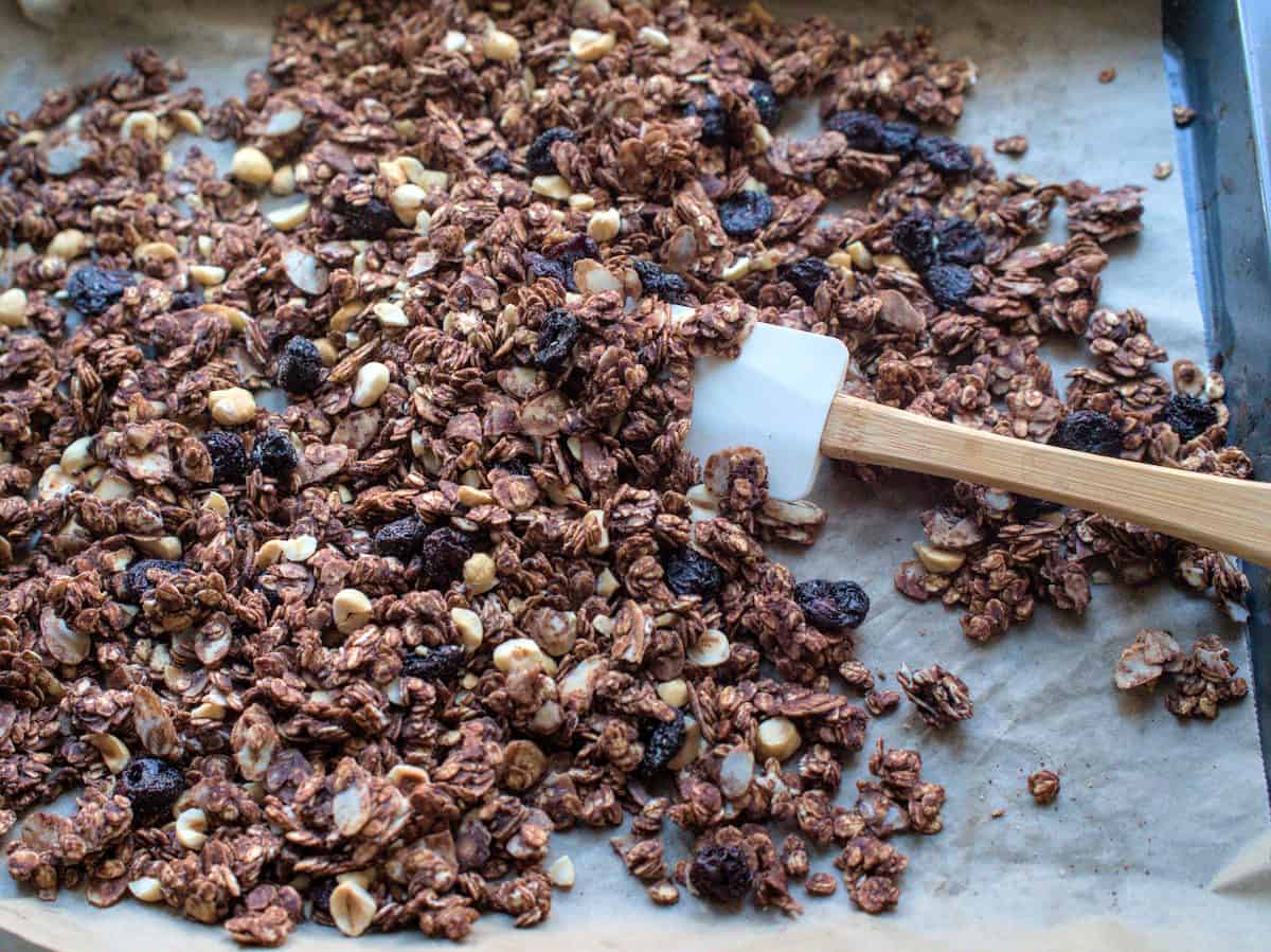 finished sourdough chocolate cherry granola on baking sheet being stirred with a white silicone spatula
