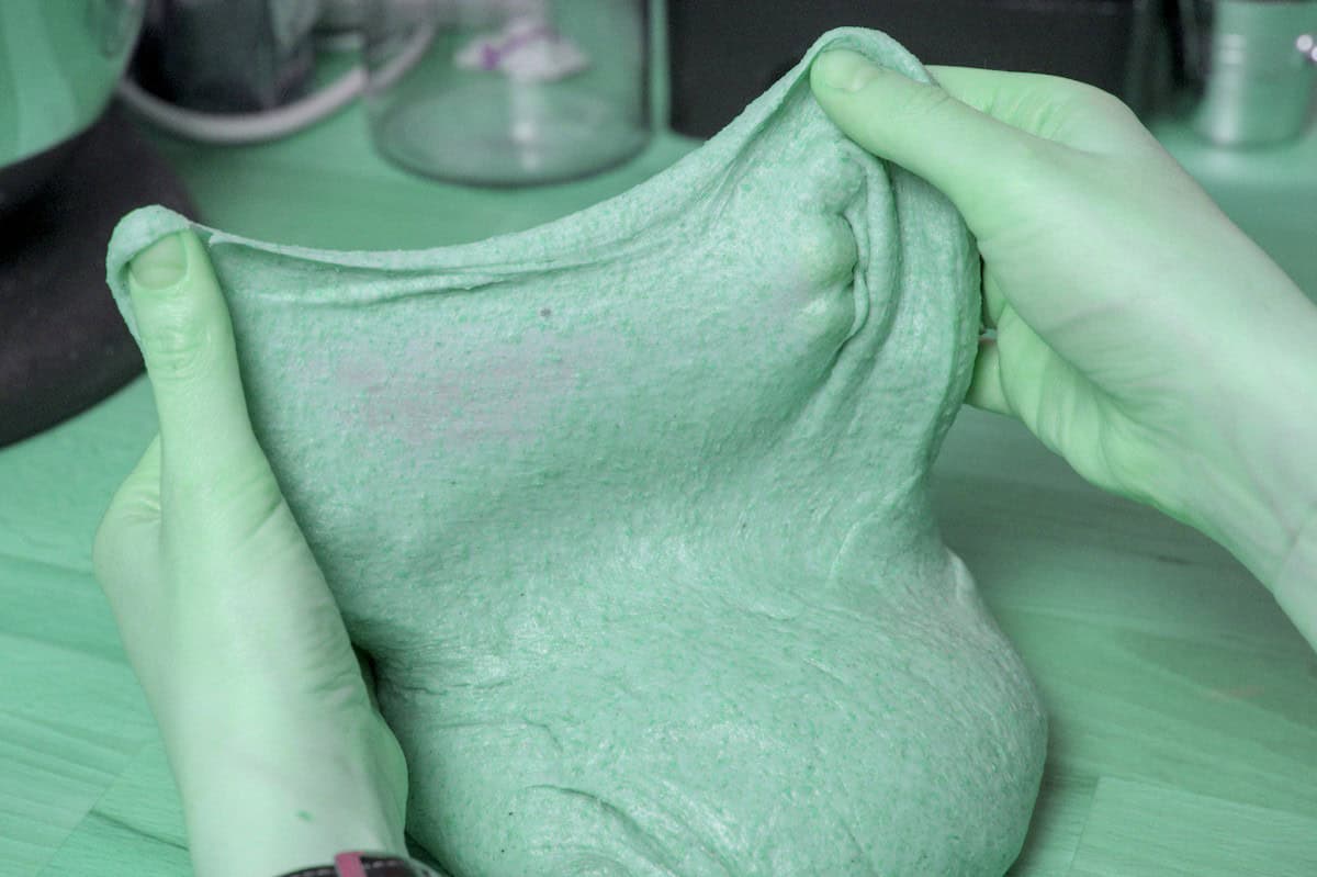 two hands stretching out the spelt brioche dough to show how the finished dough passes the window pane test