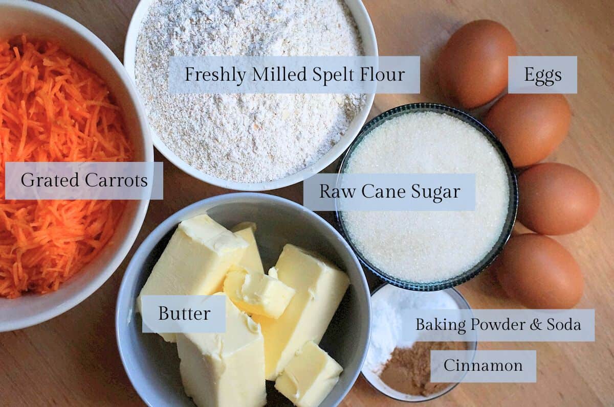 ingredients for freshly milled spelt carrot cake laid out on a wooden kitchen counter