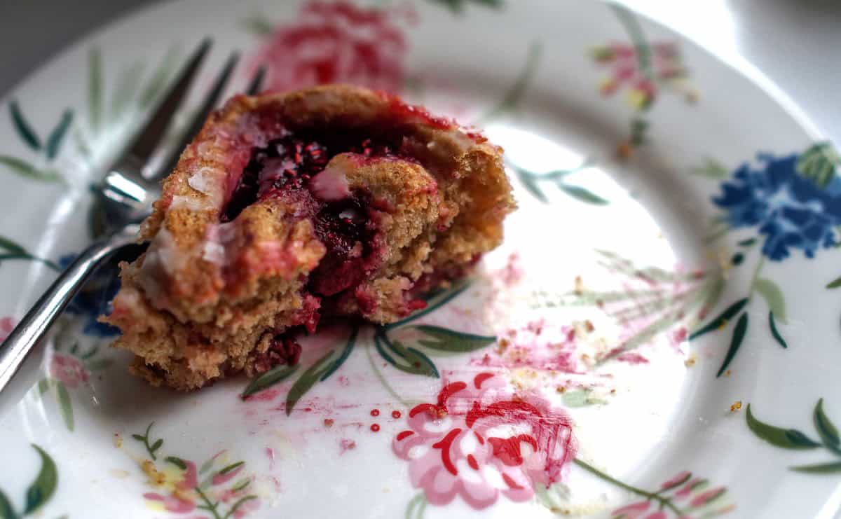 closeup of split roll on a flowery dessert plate, showcasing the flaky tender crumb and bright pink raspberry filling