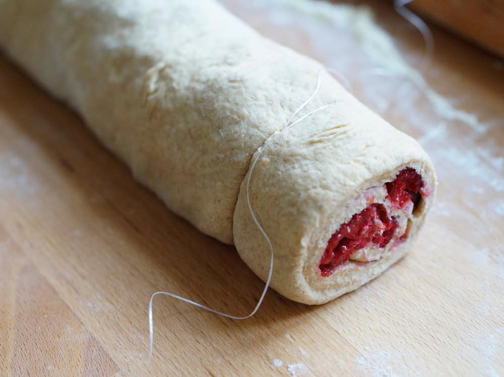 closeup of the rolled up dough being cut with a piece of dental floss, showcasing the raspberry filling