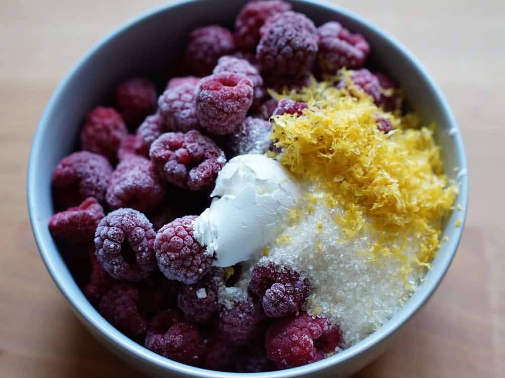 closeup of frozen raspberries, lemon zest, sugar and cornstarch in a blue bowl