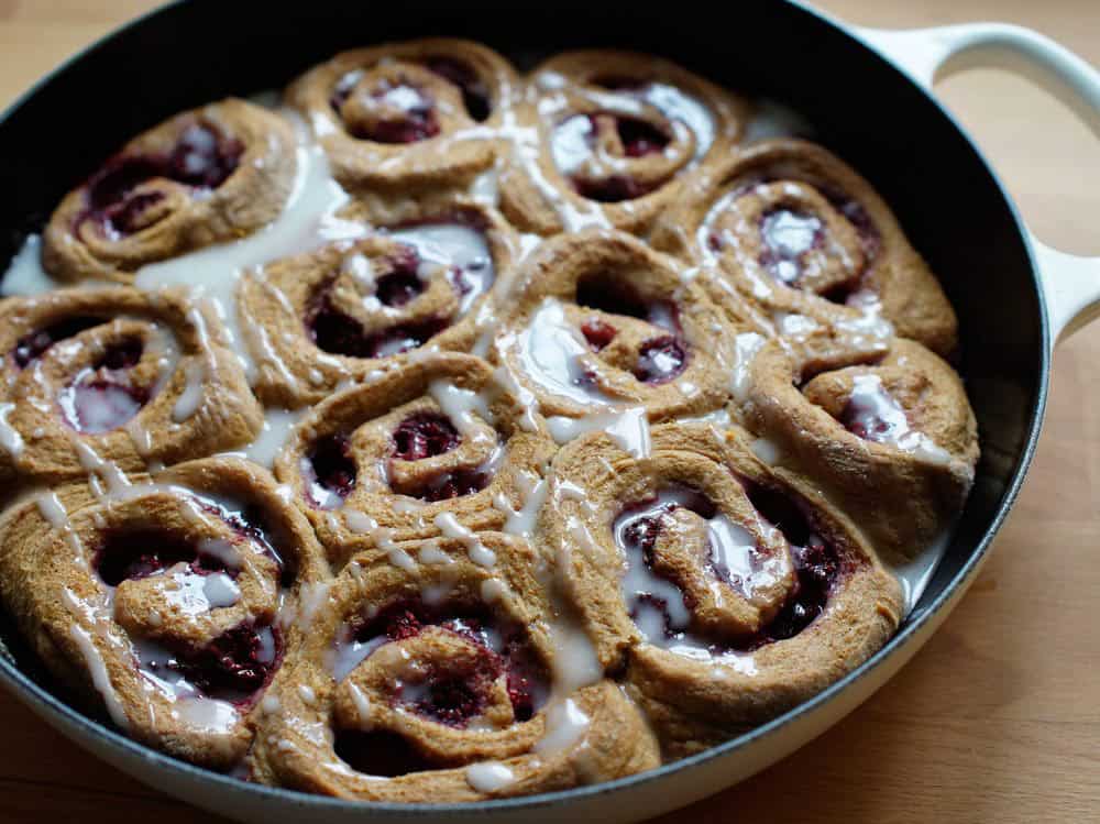 baked and glazed Lemon Raspberry Sourdough Sweet Rolls in a white cast iron pan topped with white lemon glaze