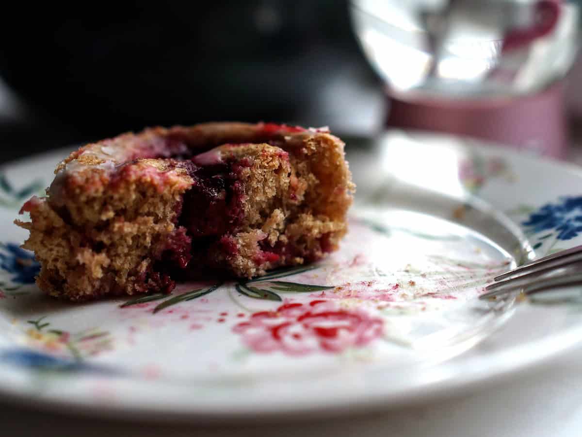 closeup of split roll on a flowery dessert plate, showcasing the flaky tender crumb and deep red raspberry filling
