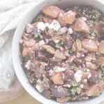 A close-up of a vibrant roasted beet and blood orange salad served on a bed of cooked Einkorn, nestled in a blue bowl and surrounded by a patterned tea towel.