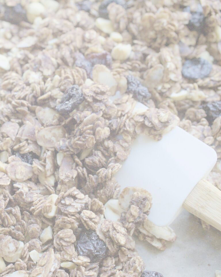 closeup of crunchy sourdough granola on a baking sheet, being turned by a white rubber spatula