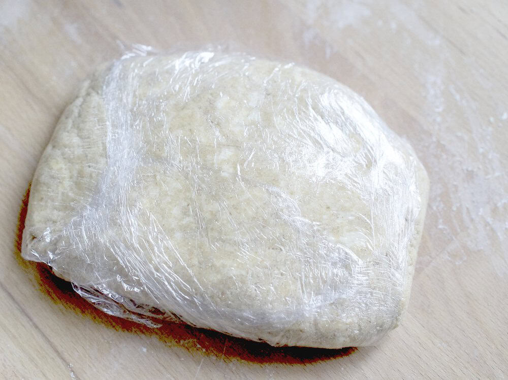 closeup of finished sourdough pie crust dough wrapped in plastic wrap