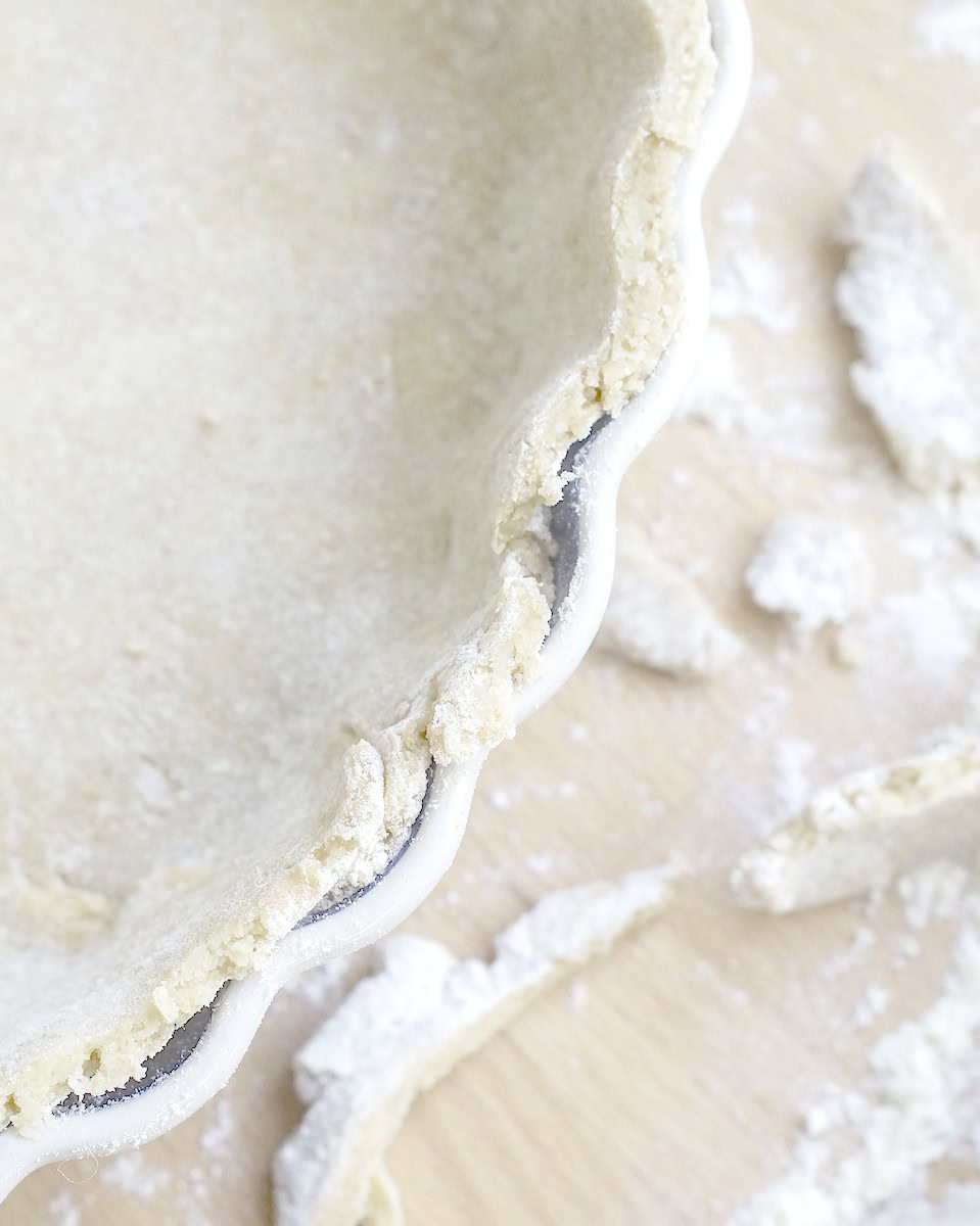 closeup of sourdough pie crust in tart pan, edges trimmed neatly with floury scraps of dough and a rolling pin next to it