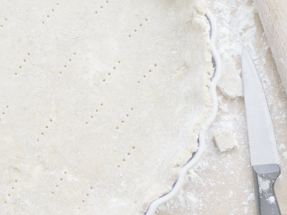 kamut pie crust draped in pie plate, visible indents of it being pricked with a fork