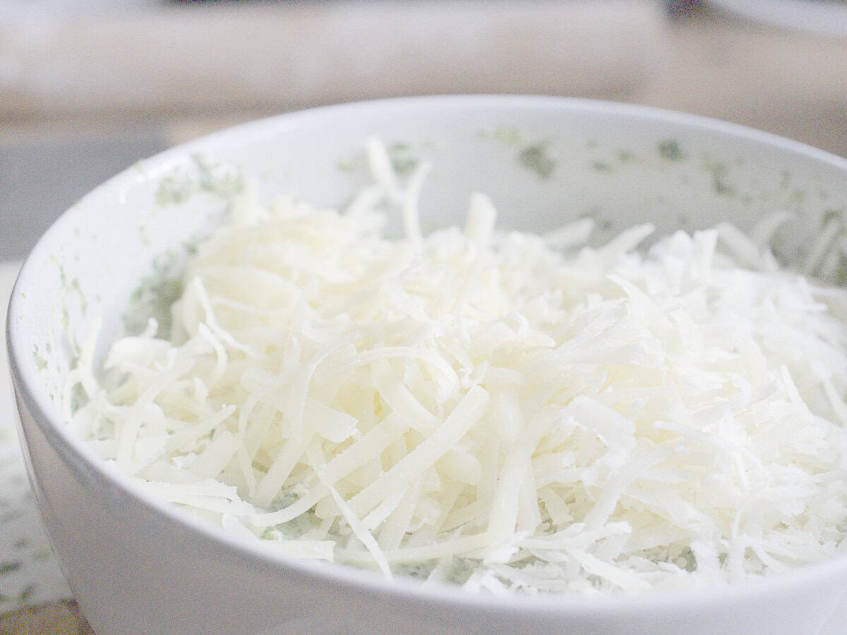 closeup of grated cheese piled up on the quiche filling being prepared in a bowl, ready to be stirred in