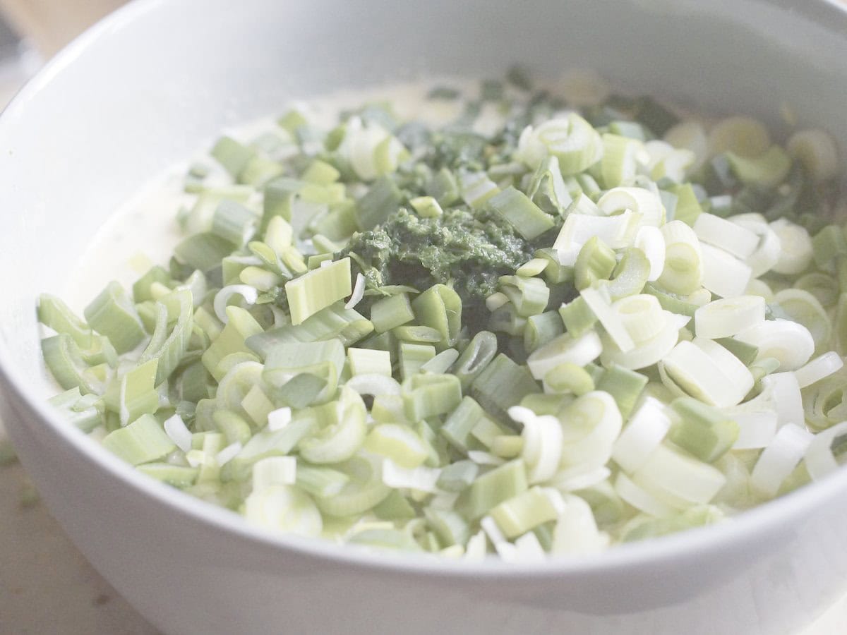closeup of thawed spinach and spring onions being piled up on the filling being prepared in a blue bowl