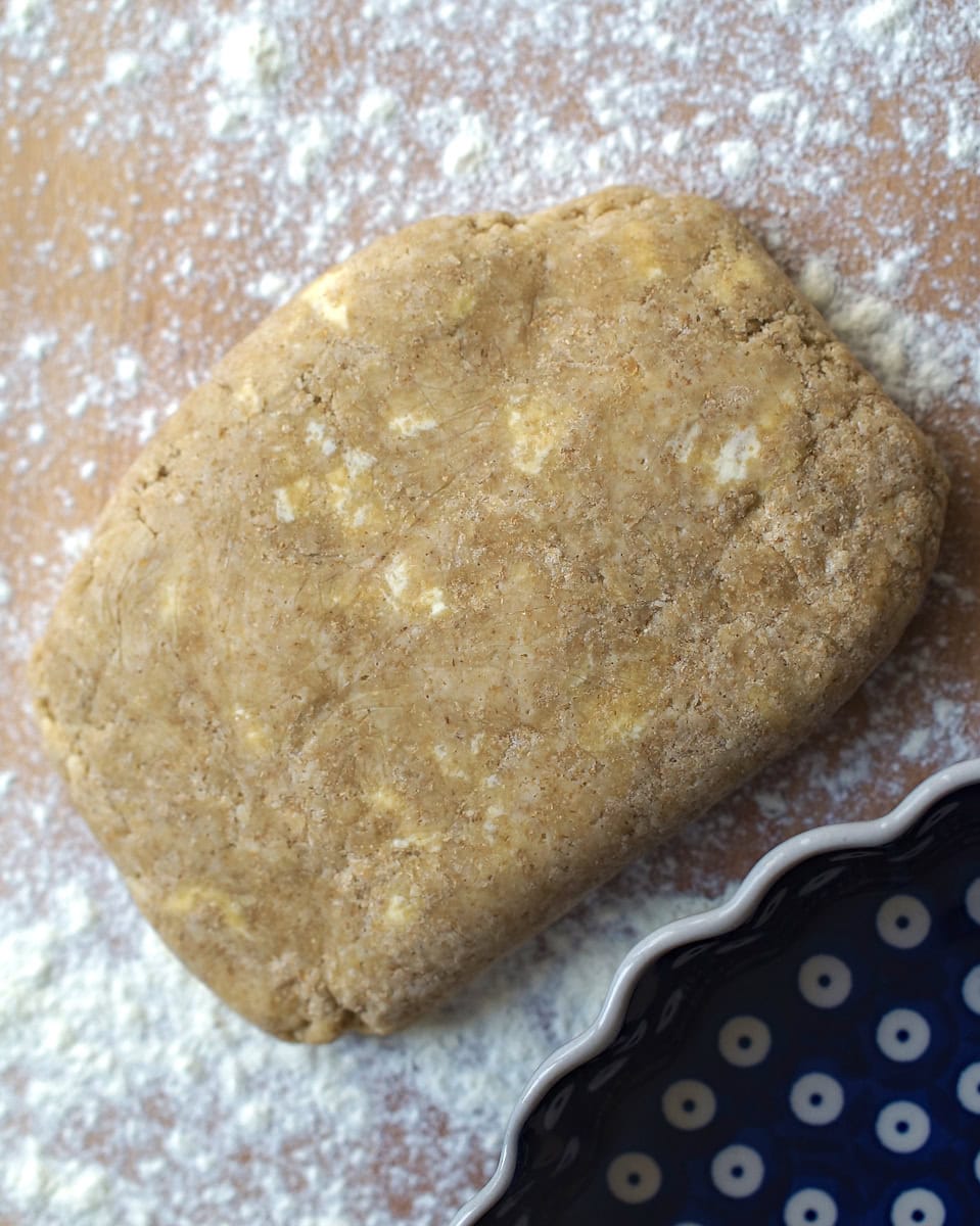 closeup of chilled sourdough pie dough on a well floured wooden surface, blue and white plate visible in the corner