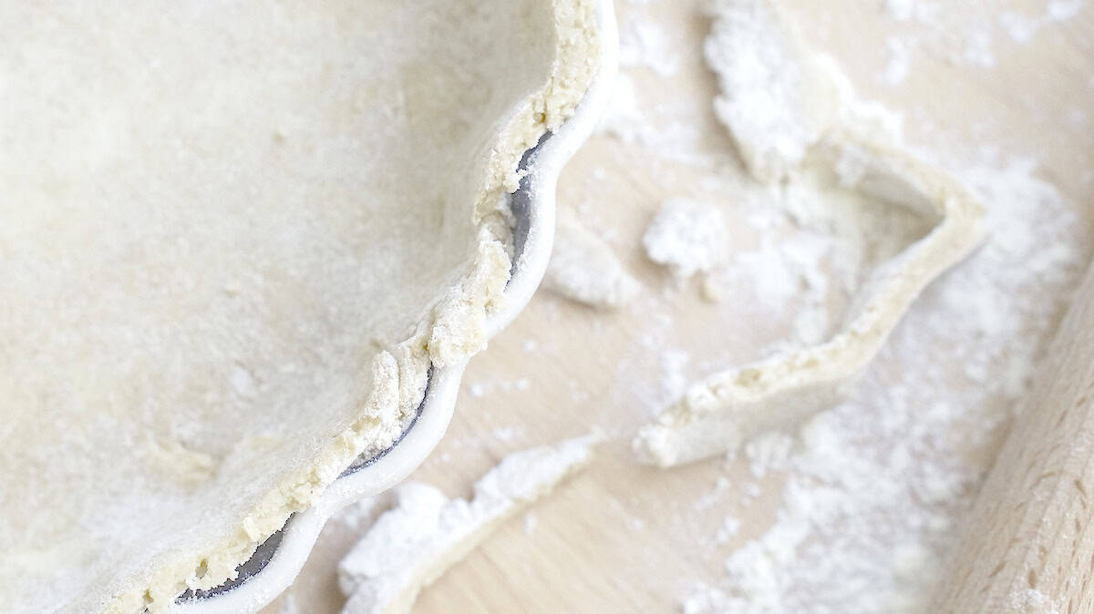 closeup of sourdough pie crust in tart pan, edges trimmed neatly with floury scraps of dough and a rolling pin next to it