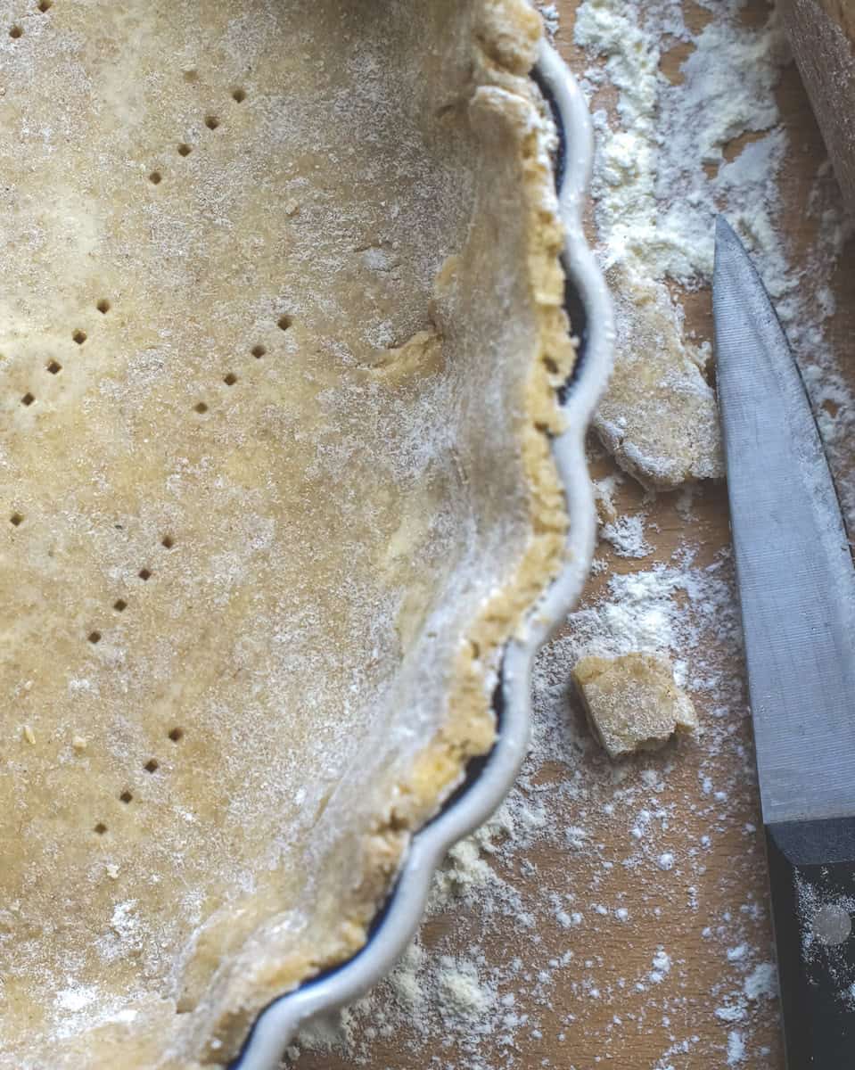 easiest sourdough pie crust draped in pie plate, visible indents of it being pricked with a fork
