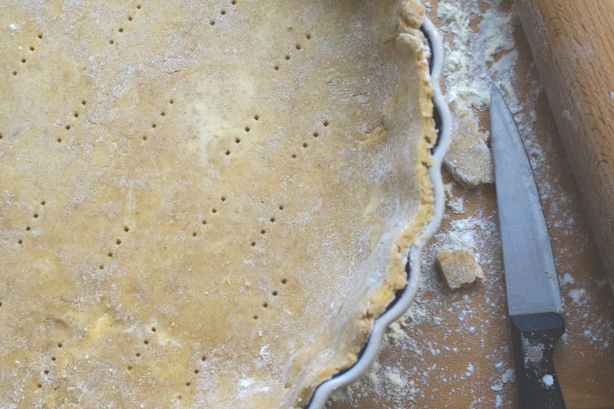 easiest sourdough pie crust draped in pie plate, visible indents of it being pricked with a fork