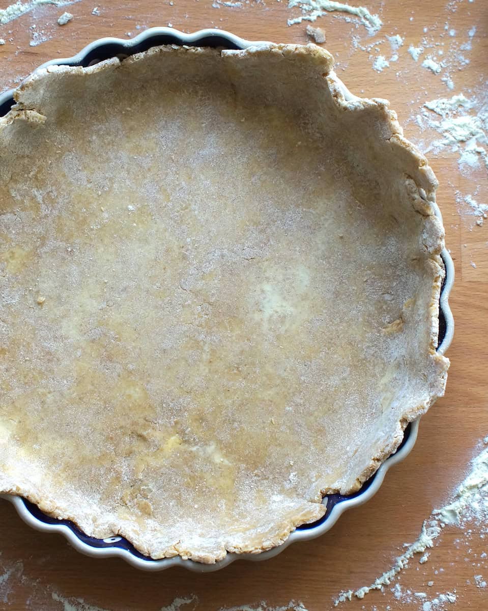 overhead shot of sourdough pie dough draped in pie plate, on a floured work surface.