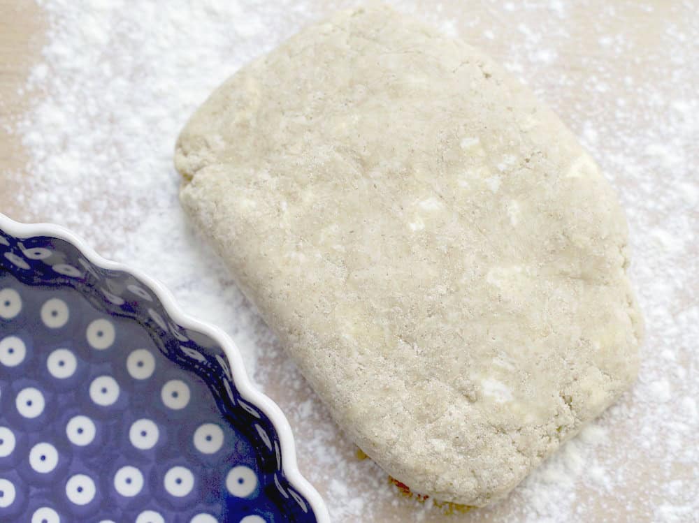 closeup of chilled sourdough pie dough on a well floured wooden surface, blue and white plate visible in the corner