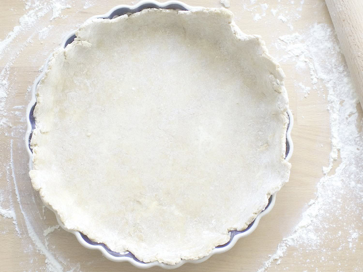 overhead shot of sourdough pie dough draped in pie plate, on a floured work surface with a rolling pin on the side