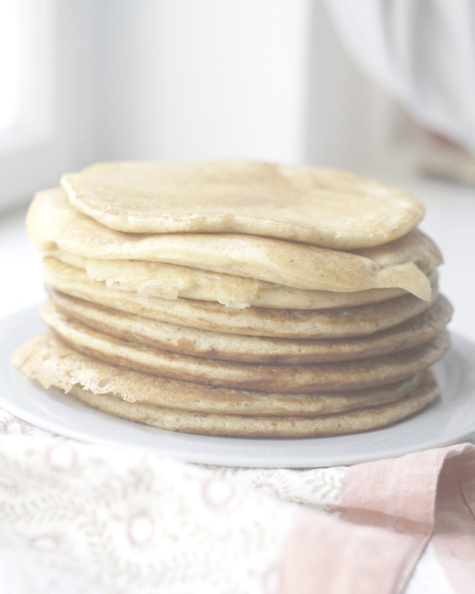 A stack of golden brown All-Discard Sourdough Pancakes on a light blue plate. Underneath is a counter with chipped white paint and a colorful tea towel to the side