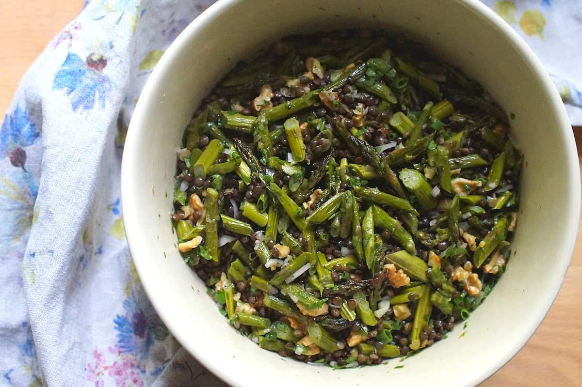 Roasted asparagus and lentil salad in a cream ceramic bowl, with a floral tea towel backdrop.