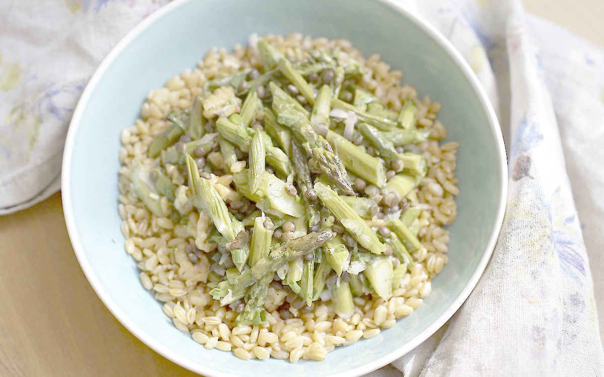 Einkorn grain bowl with roasted asparagus, black beluga lentils, and toasted walnuts on a blue plate.