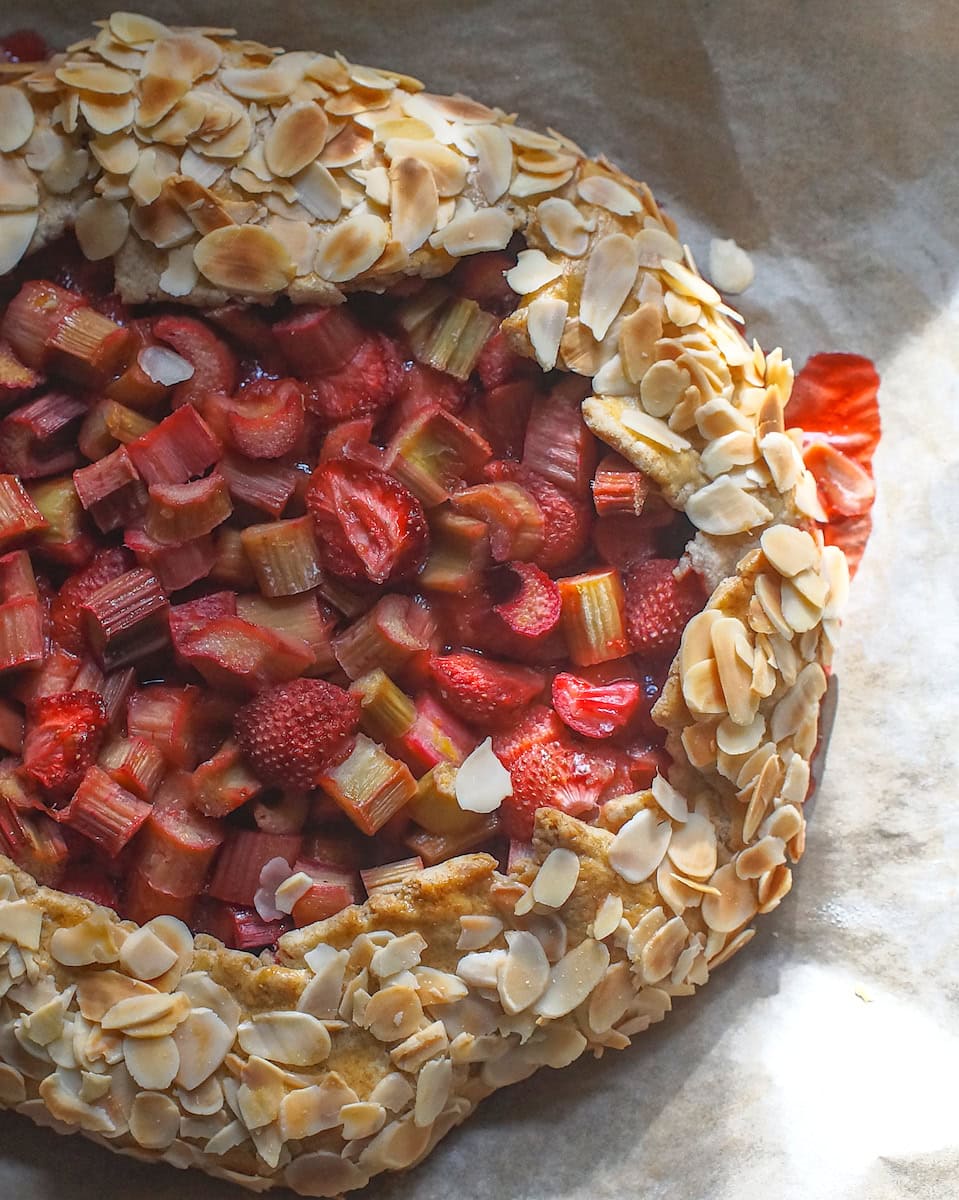 Overhead shot of Rhubarb, Strawberry and Almond Sourdough Galette, on a lined baking sheet with streaky sunlight