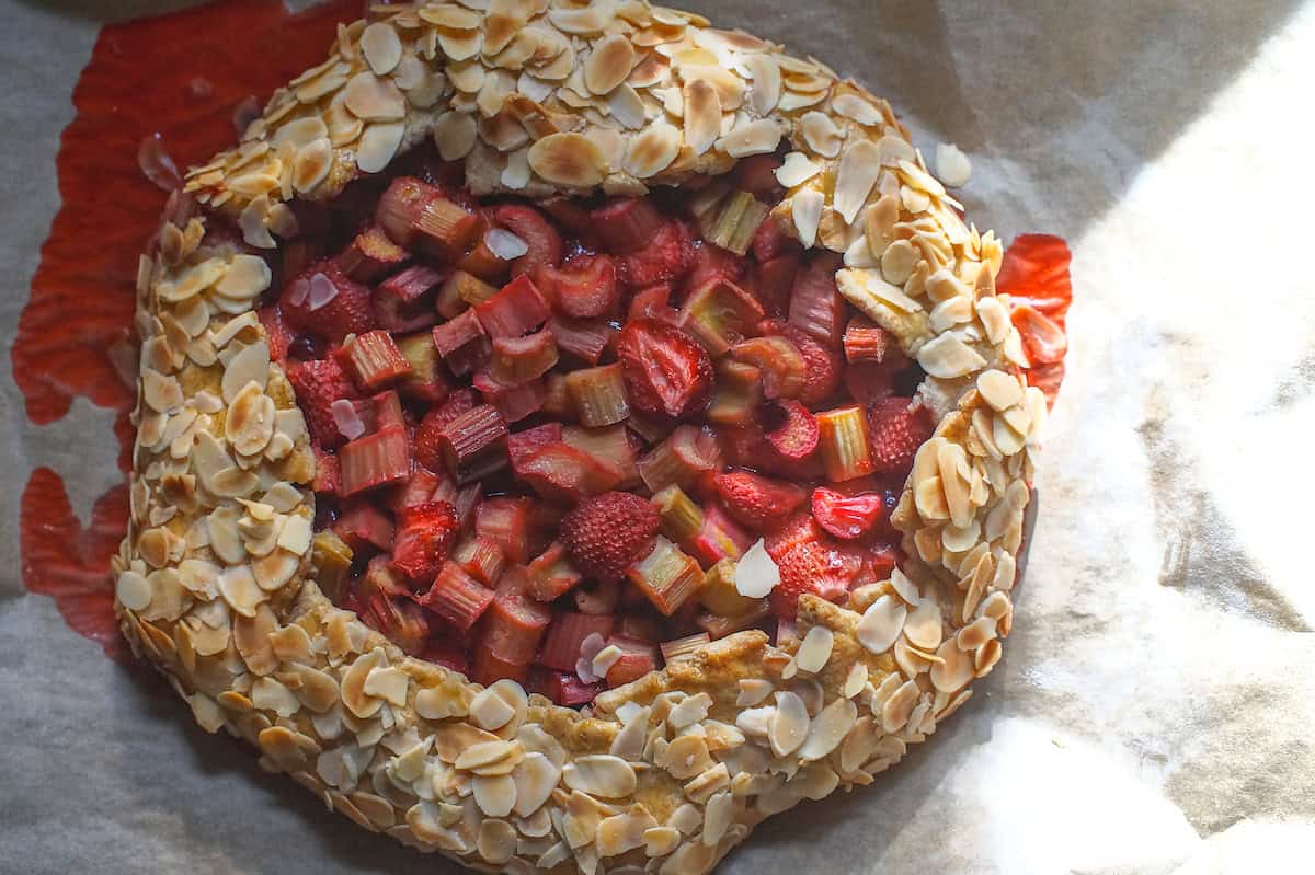 Overhead shot of Rhubarb, Strawberry and Almond Sourdough Galette, on a lined baking sheet with streaky sunlight