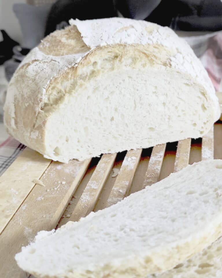 Sliced loaf of soft wheat sourdough bread made without bread flour on a wooden cutting board.