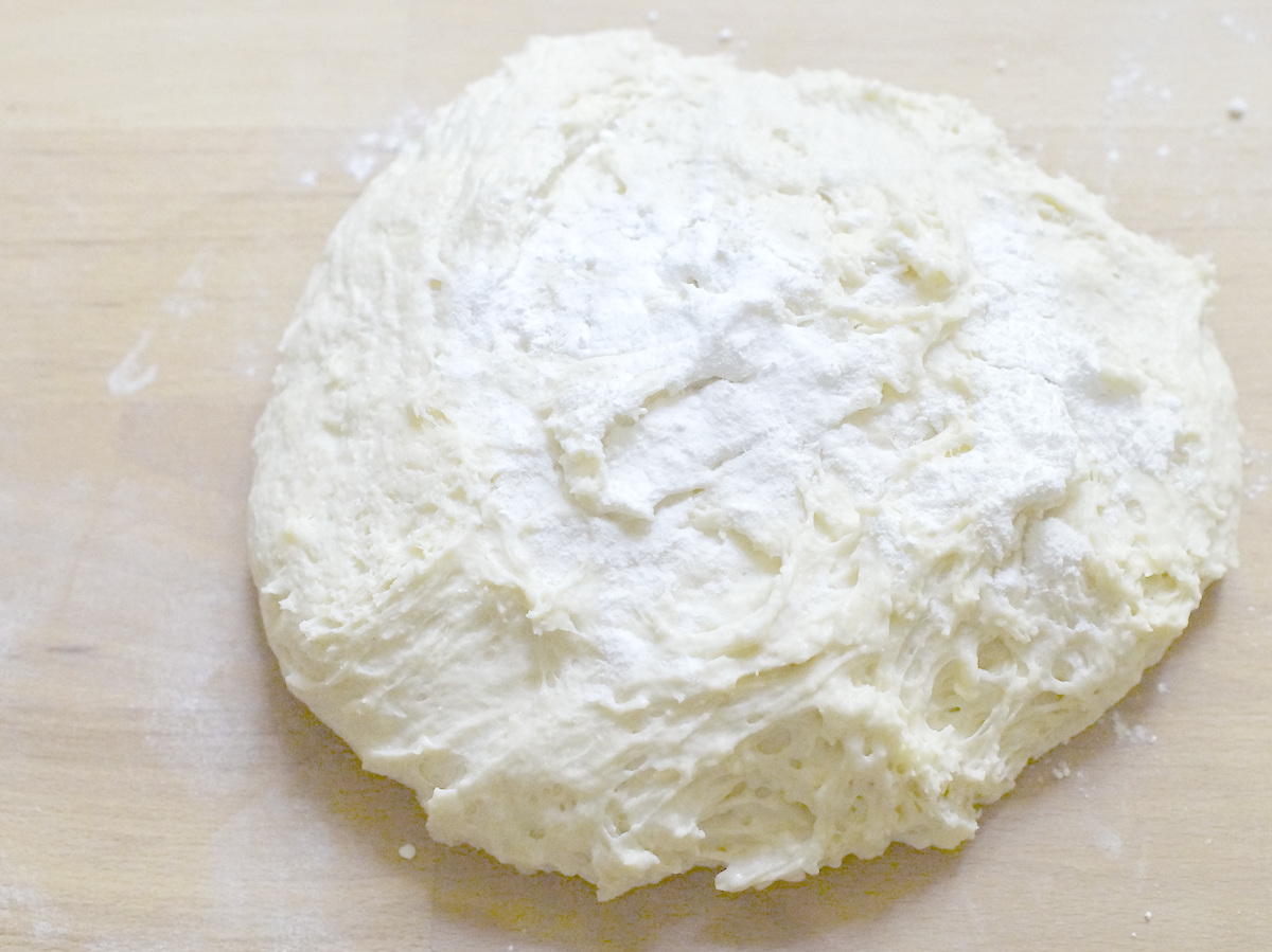 a puffy, moist sourdough discard dough, resting on a warm wooden counter. The dough is flattened into a fat round, sprinkled with bakign soda and baking powder.