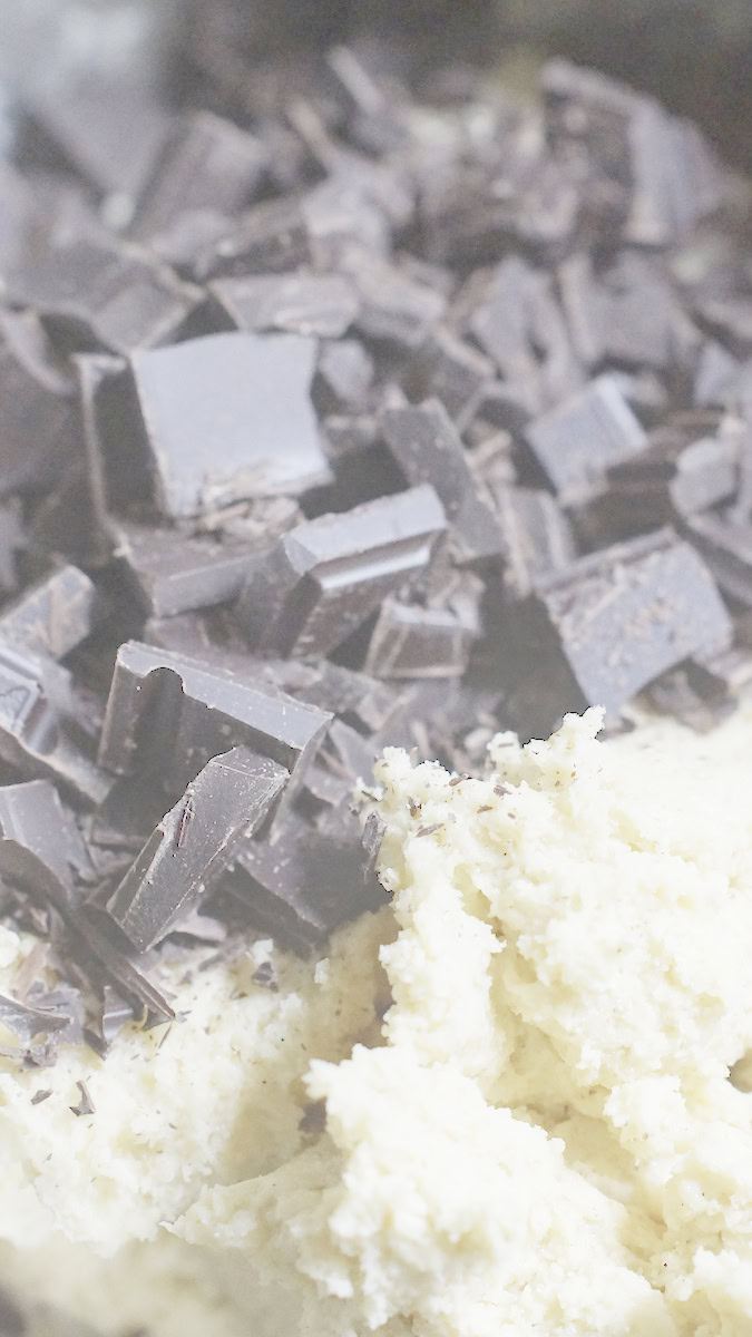A bowl of golden sourdough discard cookie dough with a large amount of chopped dark chocolate on top.
