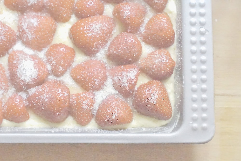 Cake pan filled with pale yellow batter, topped with halved strawberries and sprinkled generously with sugar.