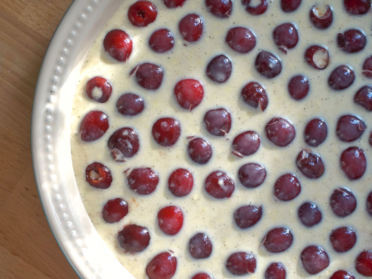 Dark red cherries in a pie dish, with a vanilla flecked liquid clafoutis batter poured over the top.
