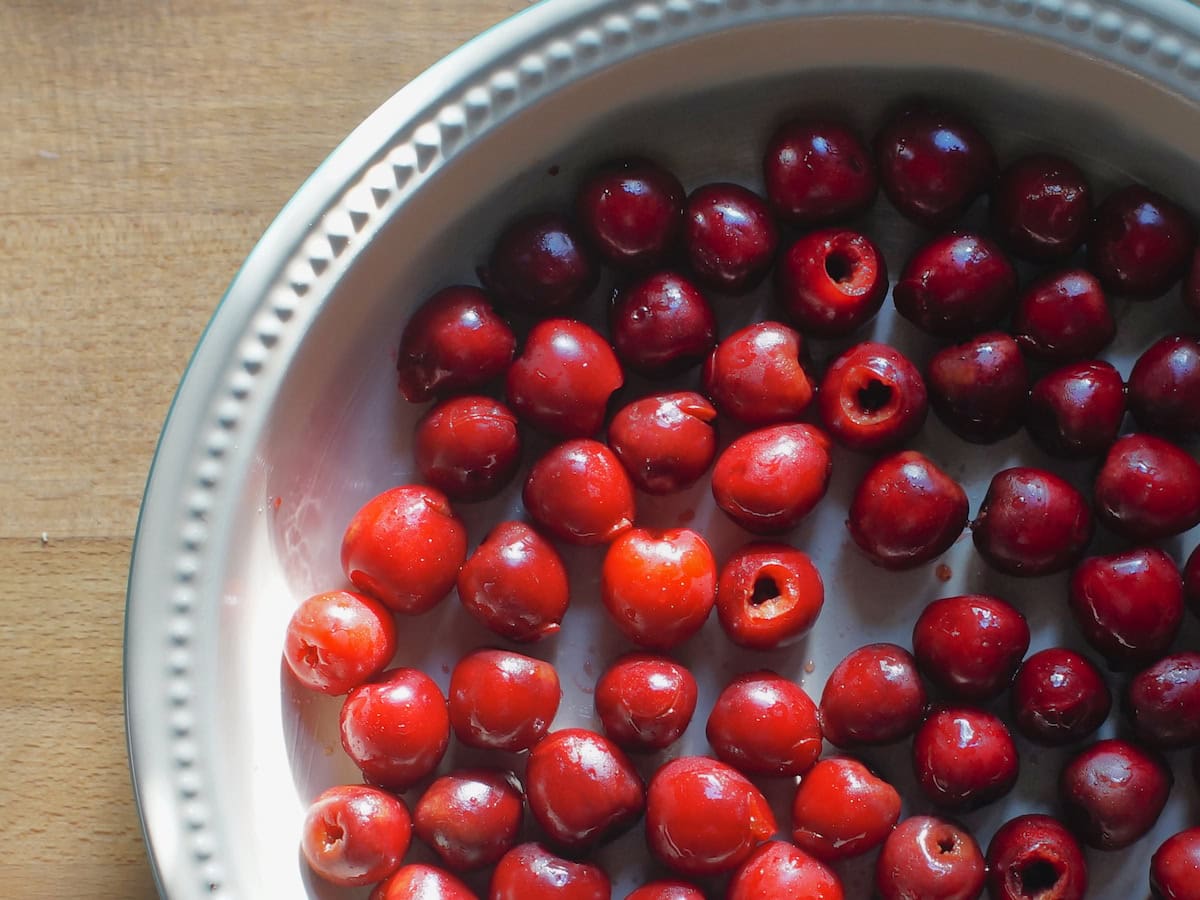 vibrant red cherries in a cream colored pie dish, shining in golden sunlight