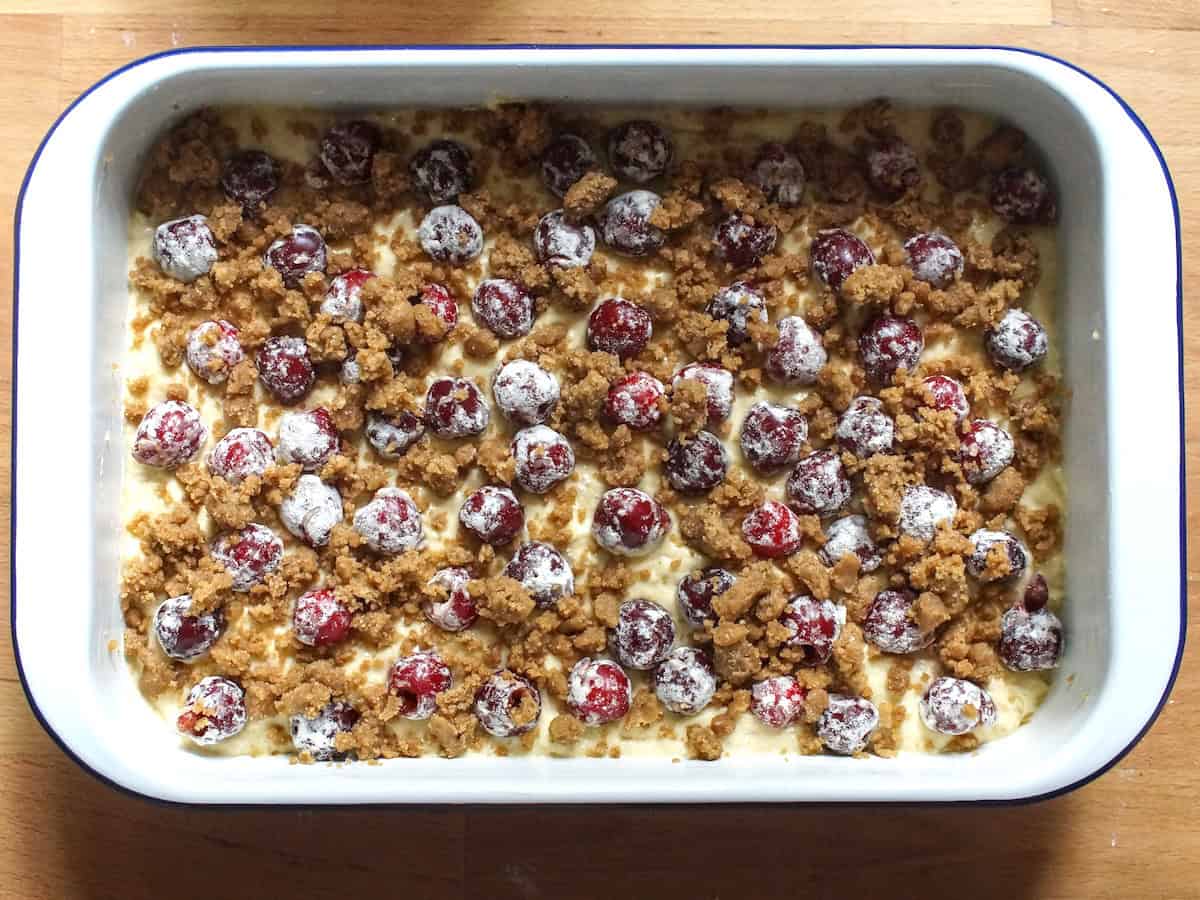 Sourdough coffee cake batter, layered into a rectangular baking pan, topped with floured cherries and crumb mixture.