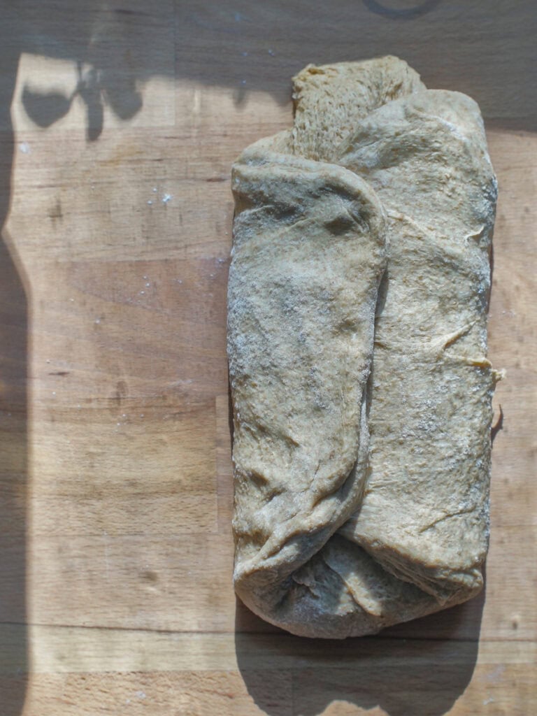 Sourdough discard sandwich bread dough sitting on a wooden counter. The edges of the dough rectangle are folded into the middle.