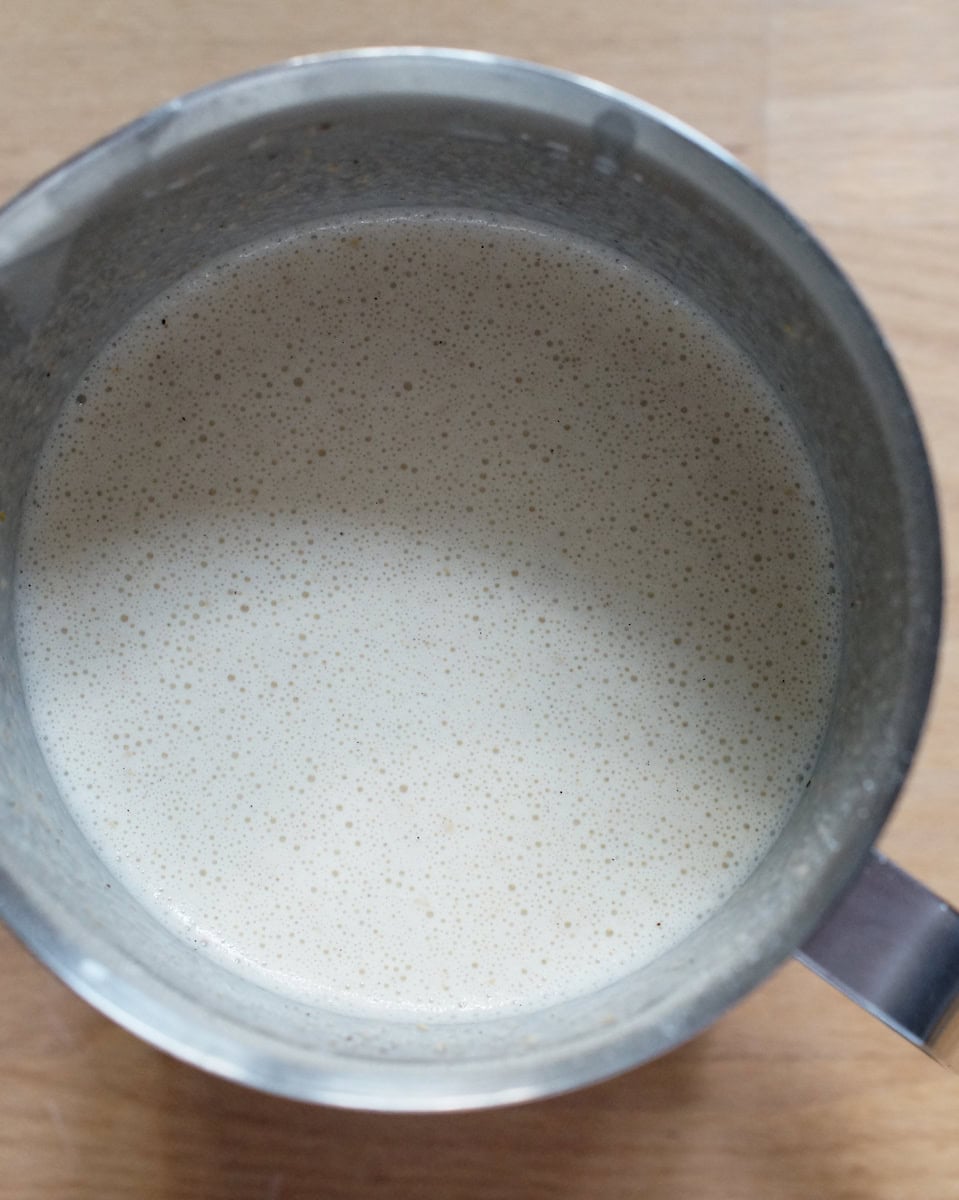 Topdown view of freshly milled einkorn clafoutis batter with tiny bubbles, resting in a metal measuring jug.