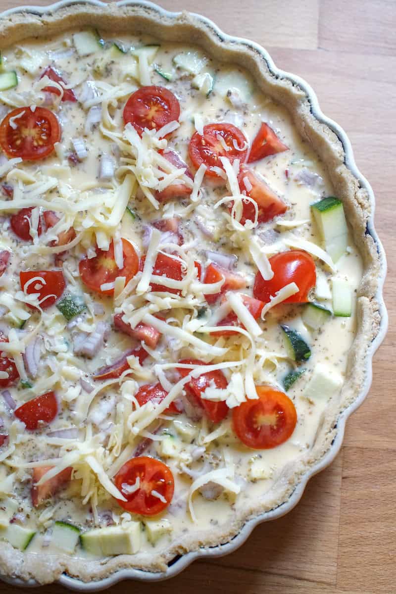 Unbaked summer veggie quiche with creamy custard, zucchini, tomatoes, shallots, and grated cheese