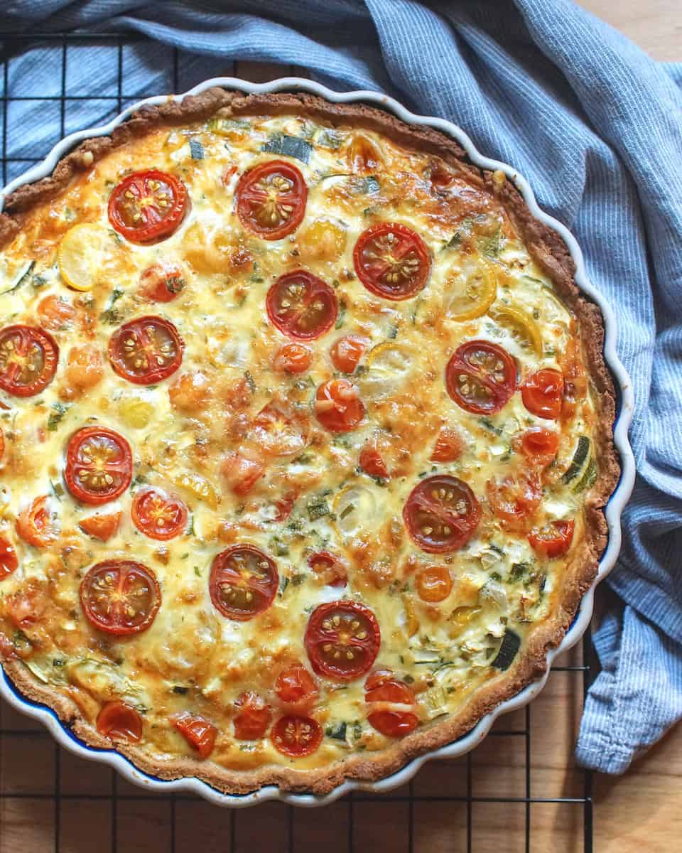 Baked summer veggie quiche with roasted tomatoes and bubbly cheese on a black wire rack