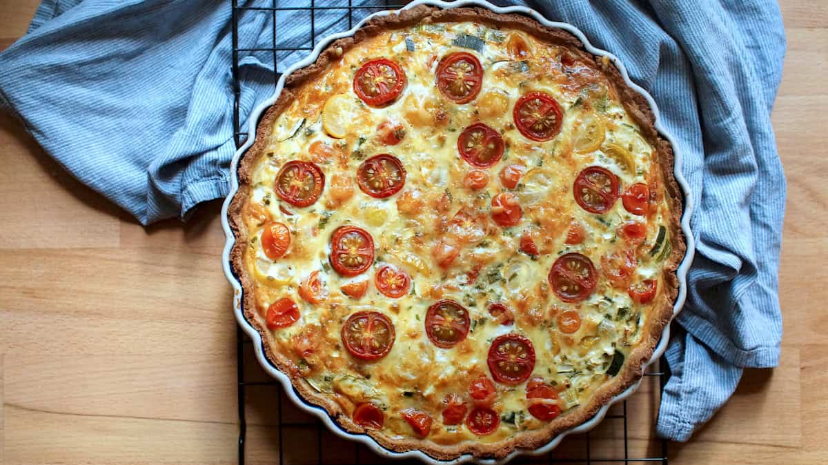 Baked summer veggie quiche with roasted tomatoes and bubbly cheese on a black wire rack