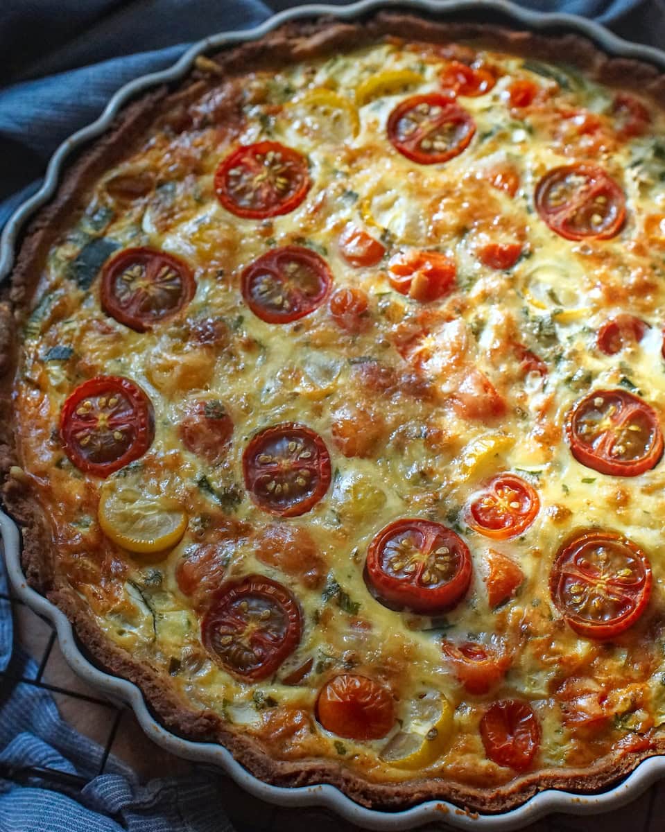 Baked summer veggie quiche with roasted tomatoes, cheese, and a golden crust, cooling on a wire rack.