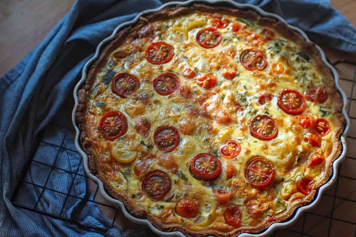 Baked summer veggie quiche with roasted tomatoes, cheese, and a golden crust, cooling on a wire rack.