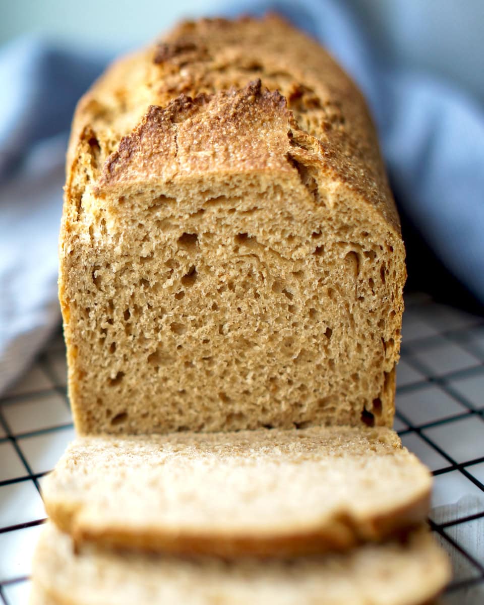 Frontal shot of sliced sourdough kamut sandwich bread, showing the even, soft crumb and rustic crust. Several slices are stacked before the loaf.