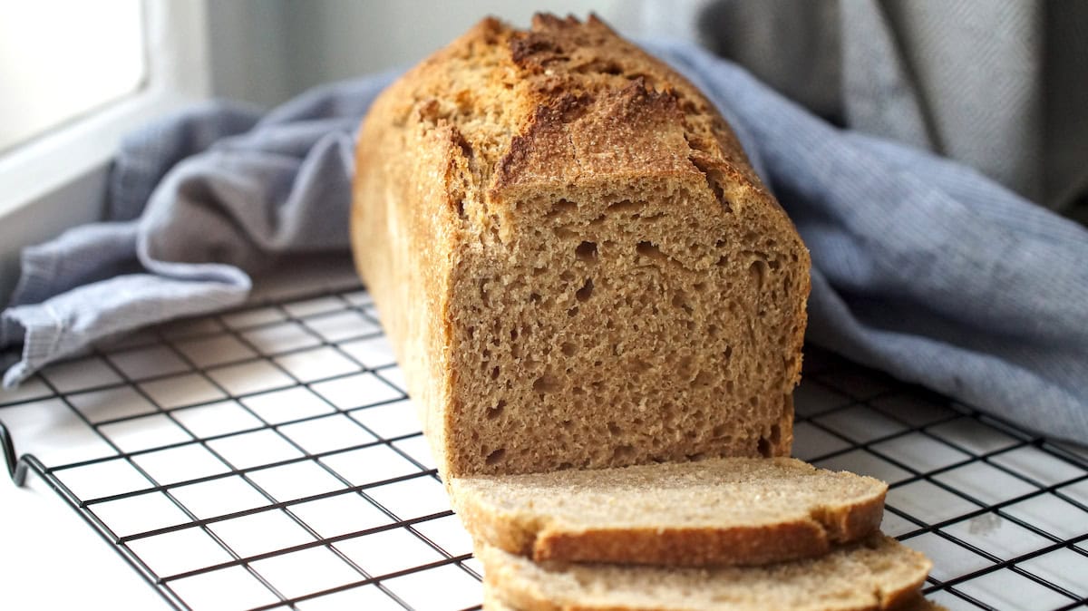 Soft and golden sourdough kamut sandwich bread has been sliced and is resting on a black cooling rack. The crumb is even, soft and golden.