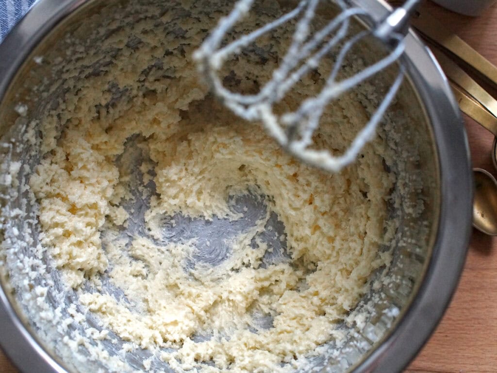 Butter and sugar have been beaten in a stainless steel bowl until pale and fluffy.