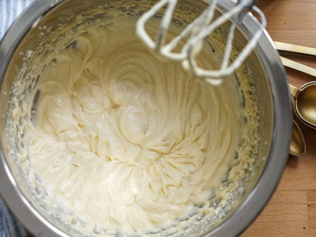 Wet ingredients are mixed into a velvety batter. The trail of the whisks has left ribbons throughout the pale yellow batter.