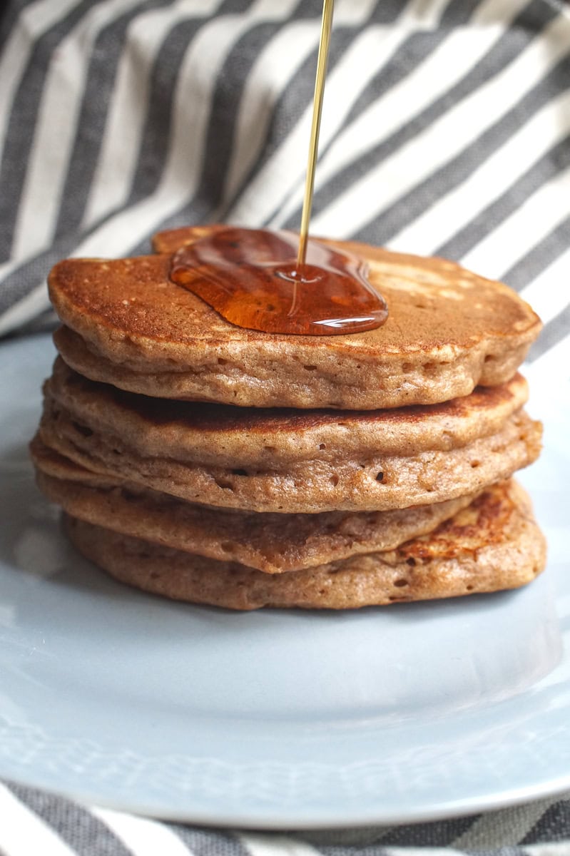 A stack of pancakes with maple syrup being poured from above, pooling on the top.
