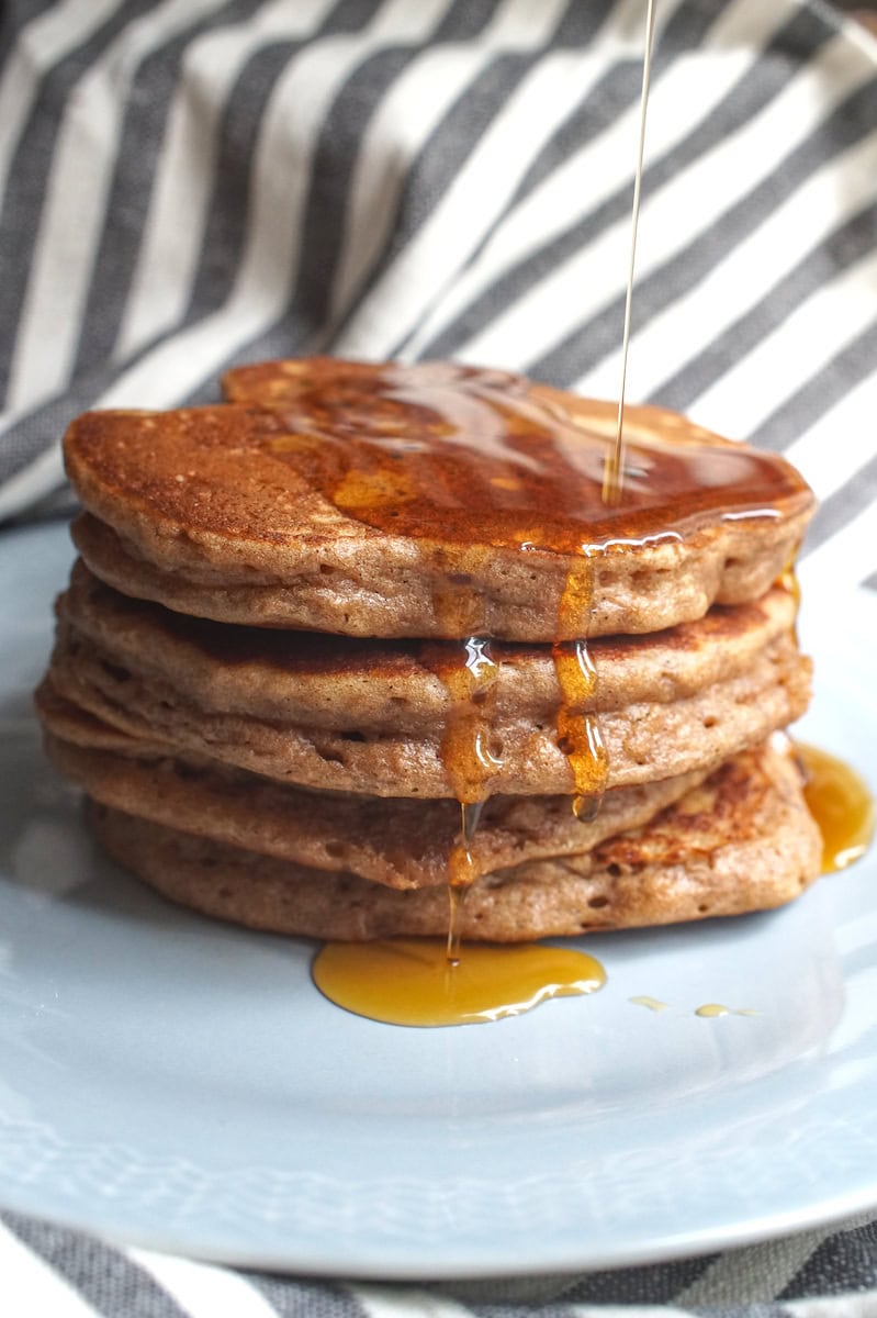 A stack of pancakes with maple syrup being poured from above, dripping down the sides.