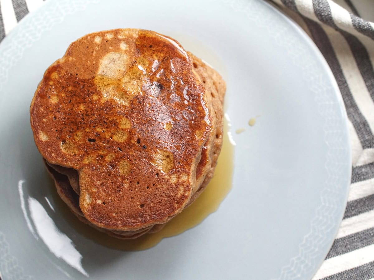 Overhead shot of a stack of dark golden brown gingerbread-spiced einkorn pancakes, drizzled with maple syrup.