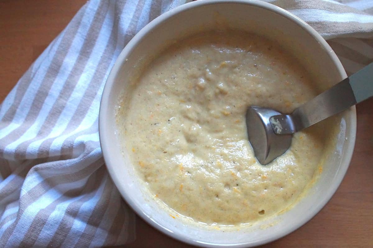 Thick, lumpy gluten-free pancake batter in a bowl with a quarter-cup measure dunked into it, showing the thick, bubbly texture.